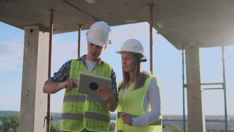 Professional-engineers-in-safety-vests-and-helmets-working-with-digital-tablet-and-blueprints